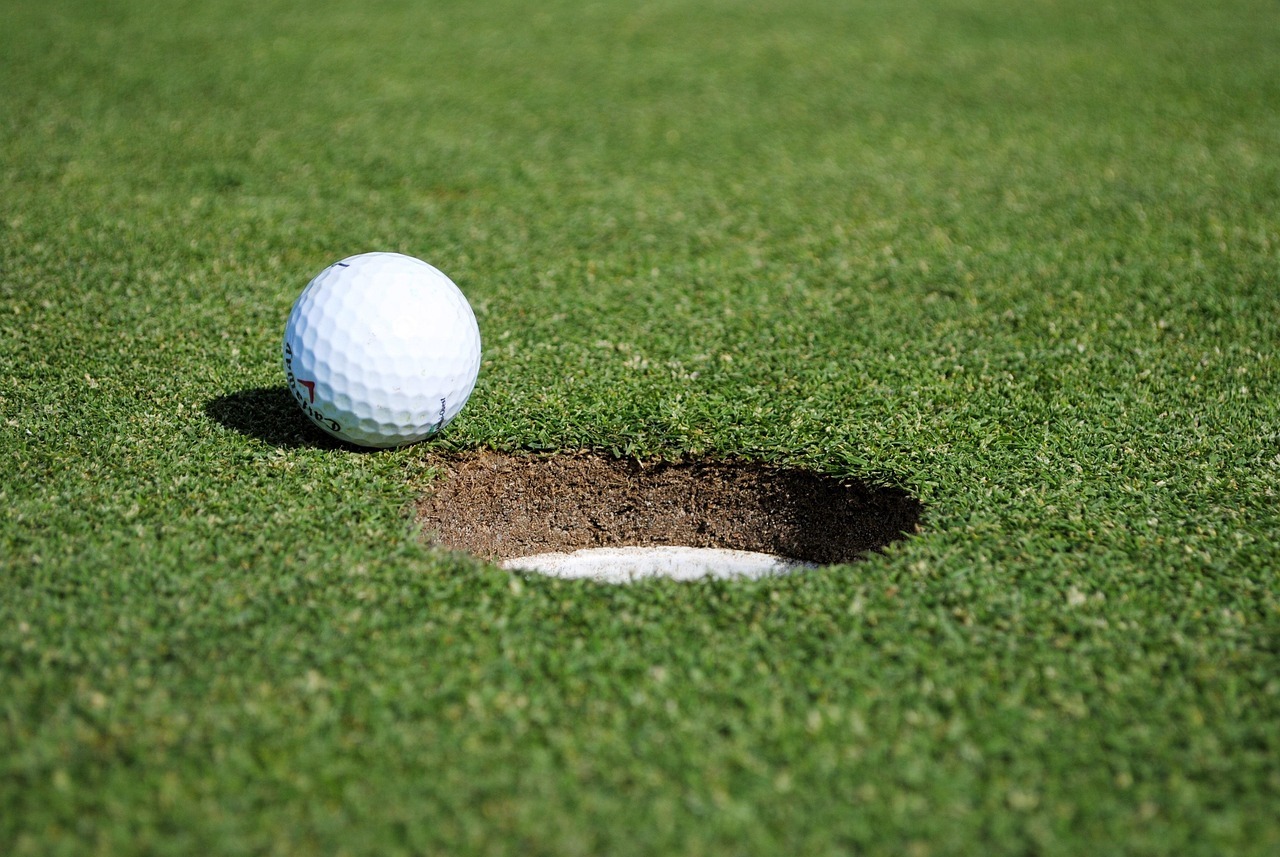 Golf ball poised near the hole on a well-manicured green, illustrating the final approach in a golf game.
